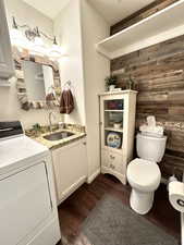 Bathroom featuring washer / dryer, toilet, wood finished floors, vanity, and wood walls