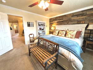 Primary Bedroom featuring ceiling fan, a textured ceiling, crown molding, carpet flooring, and wood walls