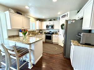 Kitchen with stainless steel appliances, a peninsula, a sink, and white cabinetry