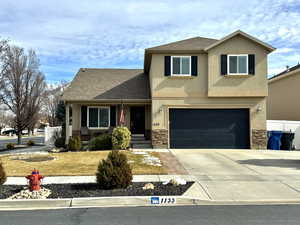 Traditional-style home with driveway, stone siding, an attached garage, and stucco siding