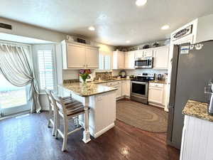 Kitchen with a breakfast bar area, appliances with stainless steel finishes, white cabinetry, dark stone countertops, and a peninsula