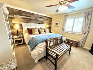 Primary bedroom featuring a textured ceiling, wood walls, visible vents, carpet, and crown molding