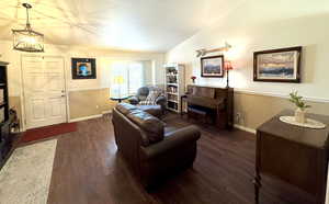 Living area featuring a notable chandelier, baseboards, vaulted ceiling, and dark wood-style flooring