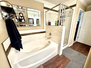 Primary Bathroom featuring wood finished floors, ornamental molding, a garden tub, and a shower stall