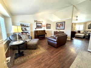 Living area with lofted ceiling, ceiling fan, dark wood-style flooring, and baseboards