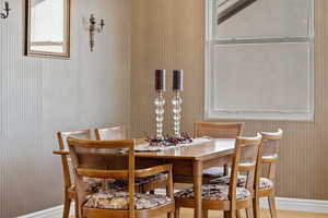 Dining area with wallpapered walls, baseboards, and wood finished floors