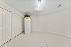 Interior space featuring baseboards, visible vents, a textured ceiling, concrete flooring, and multiple closets