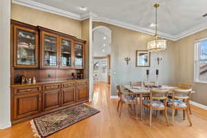 Dining room featuring arched walkways, light wood-style flooring, visible vents, a healthy amount of sunlight, and ornamental molding