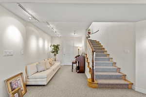 Living area with stairs, carpet, baseboards, and track lighting