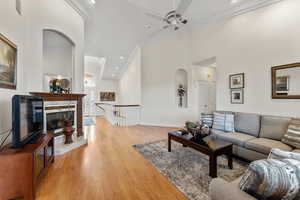 Living area featuring light wood finished floors, baseboards, arched walkways, a towering ceiling, and ornamental molding