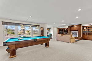 Playroom with a glass covered fireplace, pool table, light carpet, and a healthy amount of sunlight