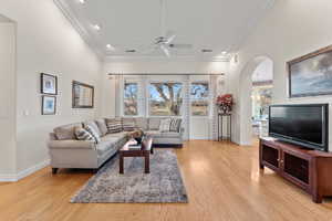 Living area with arched walkways, ornamental molding, light wood-type flooring, and visible vents