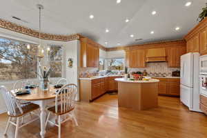 Kitchen featuring custom exhaust hood, light countertops, visible vents, a kitchen island, and white appliances