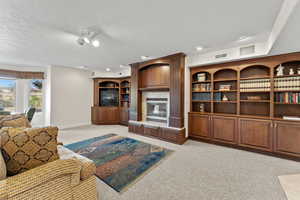 Living area featuring baseboards, visible vents, a tiled fireplace, light colored carpet, and a textured ceiling