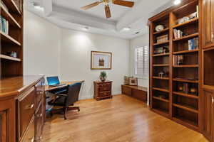 Home office with visible vents, baseboards, a raised ceiling, a ceiling fan, and light wood-style flooring