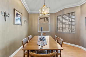 Dining space featuring baseboards, ornamental molding, light wood-style flooring, and an inviting chandelier