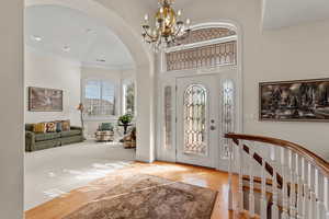 Entrance foyer with ornamental molding, arched walkways, light wood finished floors, and an inviting chandelier