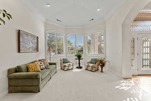 Living area with arched walkways, carpet floors, visible vents, baseboards, and ornamental molding