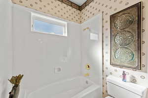 Bathroom with toilet, wallpapered walls, and shower / bathtub combination