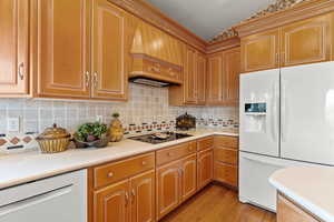 Kitchen featuring premium range hood, light countertops, white appliances, and light wood-style flooring