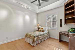 Bedroom featuring rail lighting, light wood-style flooring, baseboards, and a ceiling fan