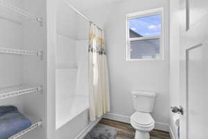 Bathroom with toilet, baseboards, shower / bath combo with shower curtain, and wood finished floors