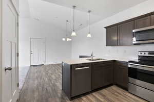 Kitchen with stainless steel appliances, light countertops, hanging light fixtures, a sink, and a peninsula