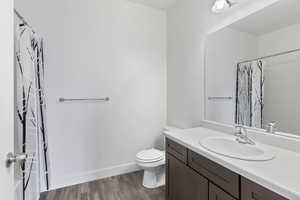 Bathroom with a shower with shower curtain, toilet, vanity, wood finished floors, and baseboards