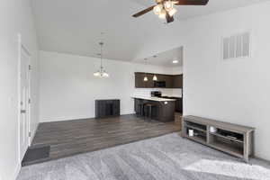 Living area featuring ceiling fan with notable chandelier, dark wood-style flooring, visible vents, and baseboards