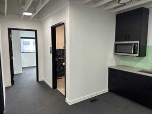 Hall with a sink, visible vents, baseboards, and dark colored carpet