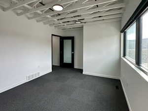 Empty room with dark colored carpet, visible vents, and baseboards