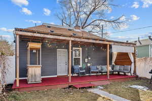 Rear view of house featuring a deck, a chimney, outdoor lounge area, and fence