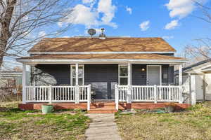 View of front facade featuring a porch, a shingled roof, and a front lawn