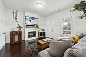 Living room featuring dark wood finished floors, visible vents, a glass covered fireplace, wainscoting, and a textured ceiling