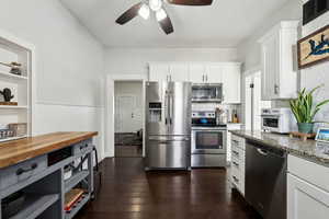 Kitchen featuring appliances with stainless steel finishes, dark stone countertops, dark wood finished floors, and white cabinets