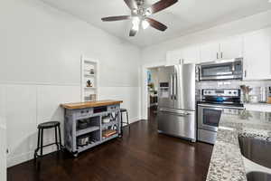 Kitchen with white cabinetry, appliances with stainless steel finishes, wainscoting, light stone countertops, and dark wood finished floors