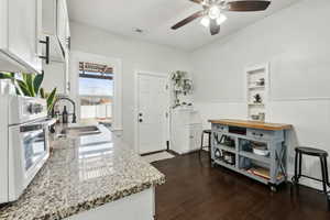 Kitchen featuring light stone counters, a sink, visible vents, white cabinets, and white oven