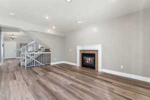 Unfurnished living room with a fireplace, wood finished floors, a chandelier, baseboards, and stairs