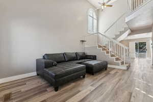 Living room with a high ceiling, wood finished floors, visible vents, baseboards, and stairs