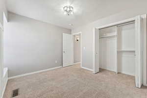 Unfurnished bedroom featuring a closet, light colored carpet, visible vents, a textured ceiling, and baseboards