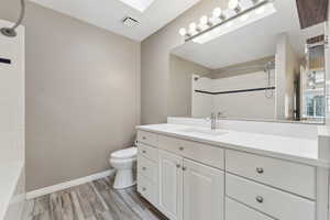 Full bath with toilet, wood finished floors, visible vents, vanity, and baseboards