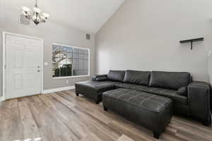 Living room with baseboards, high vaulted ceiling, an inviting chandelier, and light wood-style floors