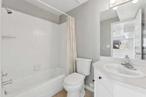 Bathroom featuring tile patterned flooring, toilet, vanity, baseboards, and shower / bathtub combination with curtain