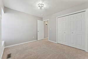 Unfurnished bedroom featuring a closet, light colored carpet, visible vents, a textured ceiling, and baseboards