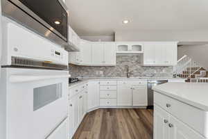 Kitchen featuring light countertops, backsplash, white cabinets, a sink, and dishwasher