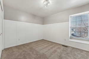 Empty room featuring light carpet, visible vents, and a decorative wall