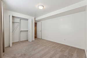 Unfurnished bedroom featuring baseboards, a closet, a textured ceiling, and light colored carpet