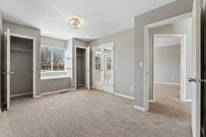 Unfurnished bedroom with a textured ceiling, light carpet, visible vents, baseboards, and multiple closets