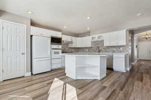 Kitchen with appliances with stainless steel finishes, a center island, light countertops, white cabinetry, and open shelves