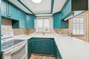 Kitchen featuring white electric stove, light countertops, a tray ceiling, and backsplash